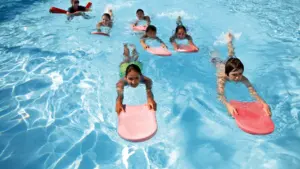 Niños aprendiendo técnicas de natación y seguridad en una piscina con tablas flotadoras.
