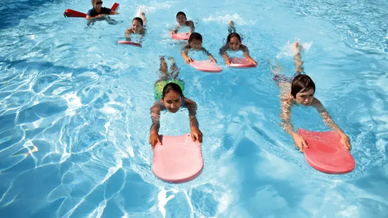 Niños aprendiendo técnicas de natación y seguridad en una piscina con tablas flotadoras.