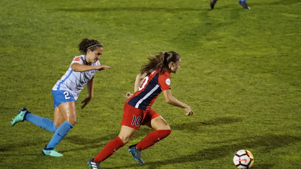 Dos futbolistas disputando un balón durante un partido en el terreno de juego.