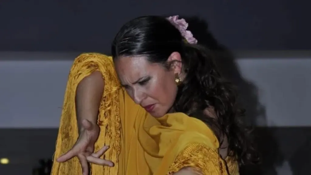 Bailarina de flamenco con vestido amarillo posando apasionadamente durante una actuación en un escenario.