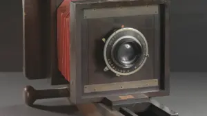 Cámara fotográfica antigua de fuelle sobre soporte de madera en un entorno de museo.