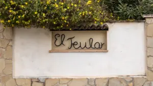 Cartel con el nombre El Teular sobre un muro de piedra en Alicante, España.
