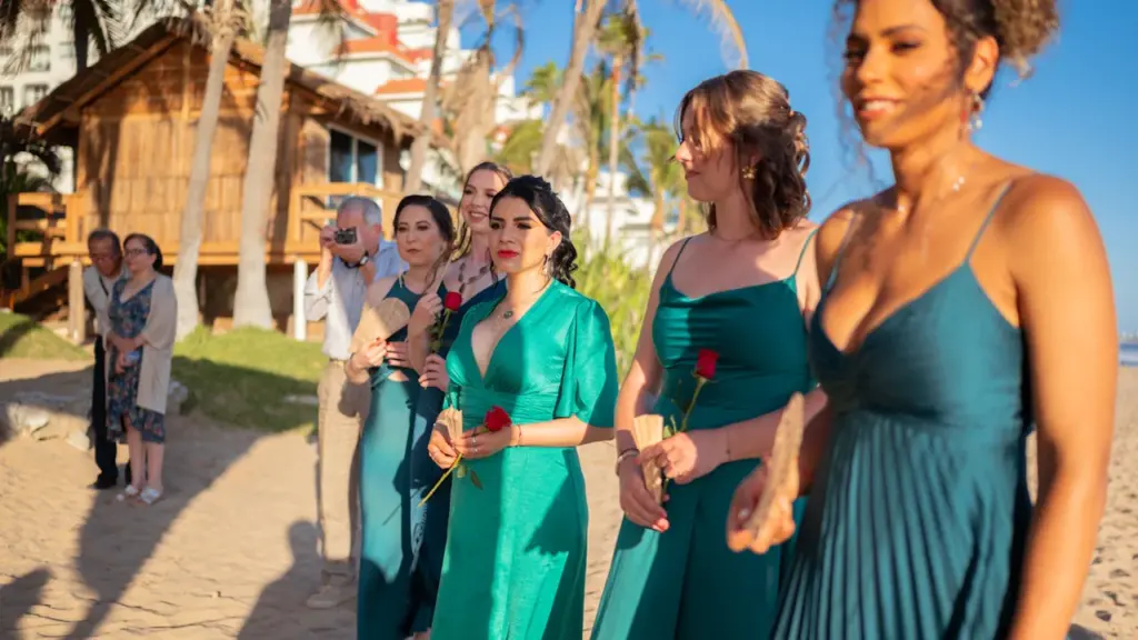 Grupo de mujeres con vestidos elegantes posando en una playa durante un día soleado.