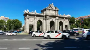 Coches y taxis circulando por la Puerta de Alcalá en Madrid durante el día.