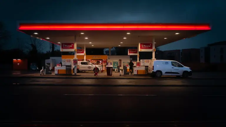 Una gasolinera moderna iluminada durante la noche con vehículos repostando combustible.