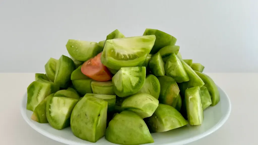 Un plato blanco lleno de tomates verdes troceados listos para una receta casera