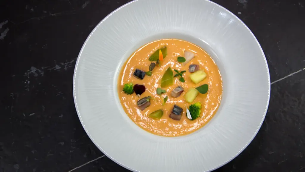 Delicioso gazpacho de tomate y aguacate servido en un elegante cuenco blanco.