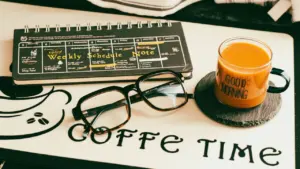 Taza de café junto a gafas y una agenda semanal sobre escritorio.