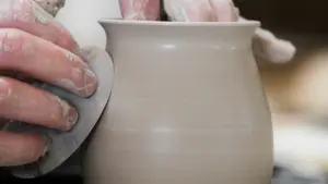 Manos de artesano cubiertas de arcilla moldeando un jarrón de cerámica en el torno.