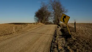 Una señal de advertencia de curva peligrosa en un camino rural de tierra.