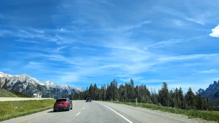 Coche conduciendo por una carretera despejada con montañas al fondo bajo cielo azul.