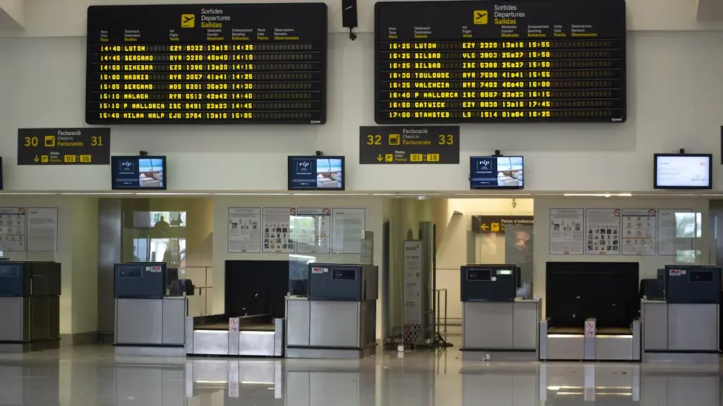 Paneles de información de salidas en un aeropuerto español con mostradores de facturación.