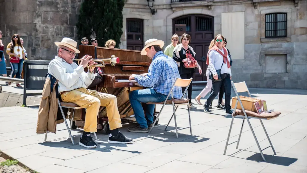 Dos músicos actuando con piano y trompeta en una plaza urbana española soleada.