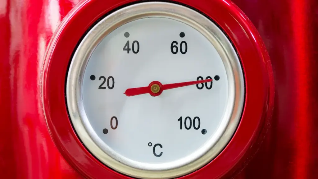 Primer plano de un termómetro analógico en un hervidor rojo marcando altas temperaturas.
