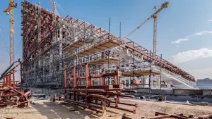 Gran estructura arquitectónica moderna en construcción con grúas bajo un cielo despejado