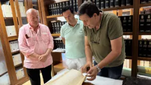 Tres hombres observan cuidadosamente un libro antiguo y desgastado en una biblioteca histórica.