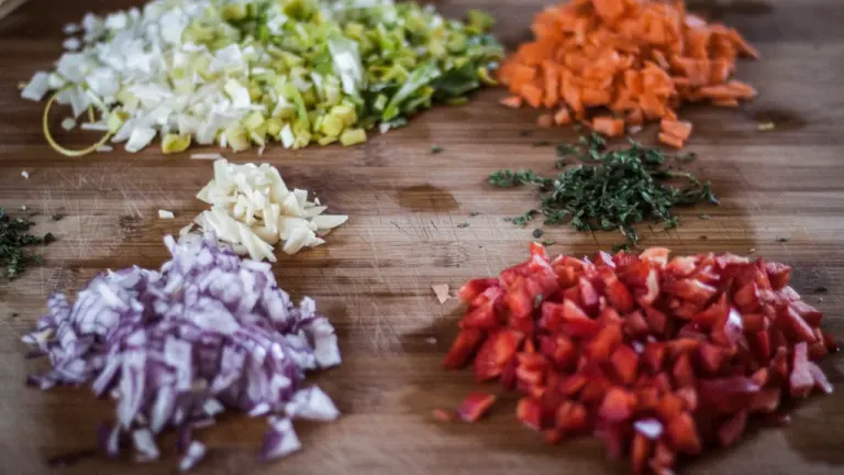 Verduras picadas como cebolla, zanahoria y pimiento sobre una tabla de madera.