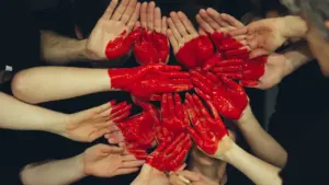 Manos unidas cubiertas de pintura roja simbolizando la solidaridad en la donación de sangre.