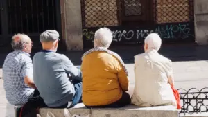 Cuatro personas mayores sentadas en un banco gris en una calle urbana española.