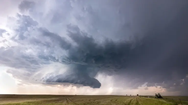 Una supercélula tormentosa se forma sobre un campo verde bajo nubes oscuras.