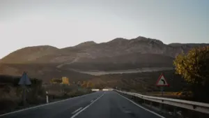 Una carretera solitaria atraviesa un paisaje árido bajo una montaña al atardecer en España.