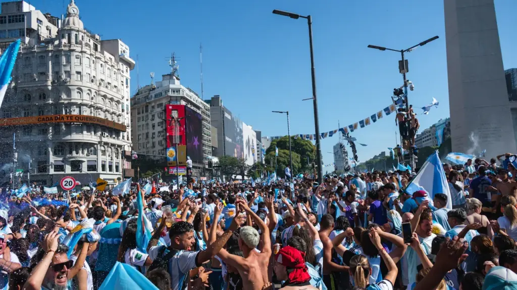 Multitud celebrando en las calles de Buenos Aires junto al Obelisco porteño con banderas argentinas.