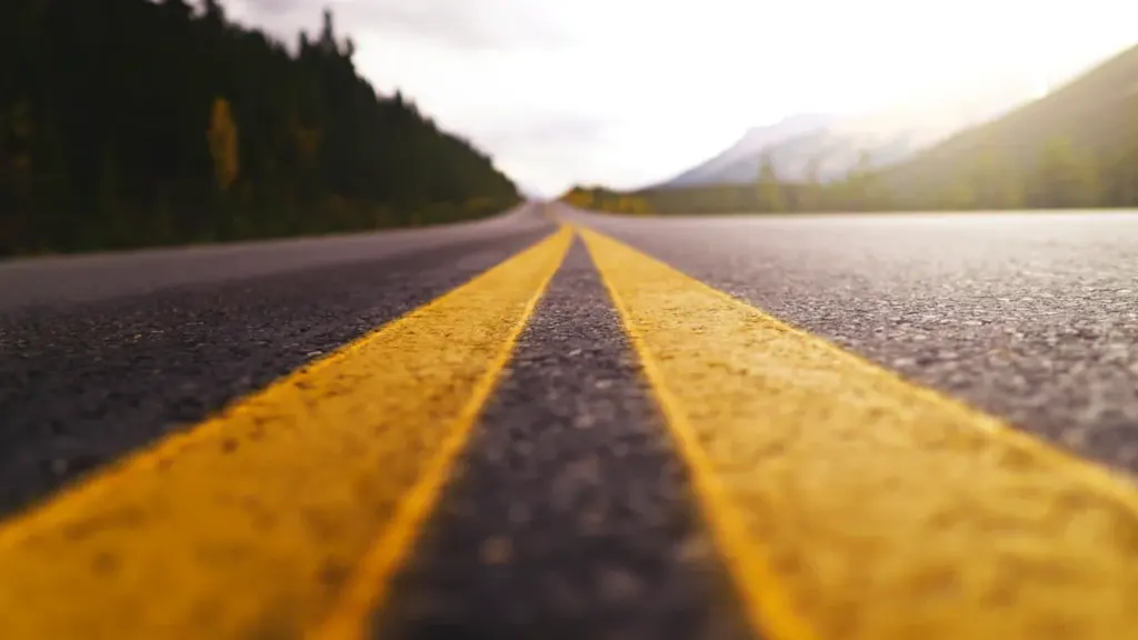 Líneas amarillas de una carretera que se adentra en un paisaje natural abierto.