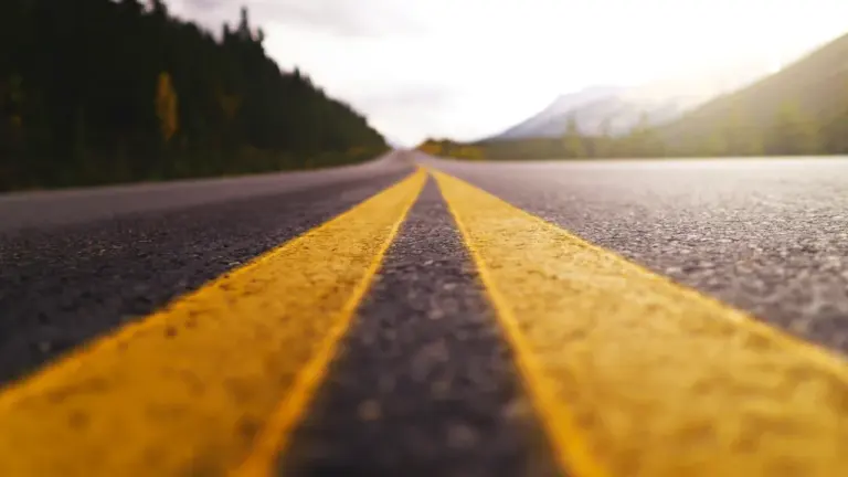 Líneas amarillas de una carretera que se adentra en un paisaje natural abierto.