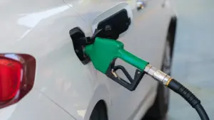 Boquilla de surtidor de gasolina introducida en el depósito de un coche blanco.