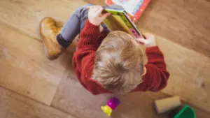 Niño pequeño sentado en el suelo leyendo un libro ilustrado en una guardería.