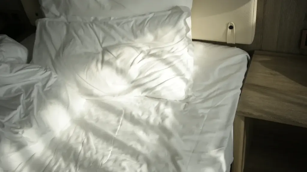 Cama de matrimonio con sábanas blancas iluminada por la luz del sol matutino.