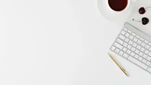 Escritorio minimalista con teclado, bolígrafo y una taza de café sobre superficie blanca.